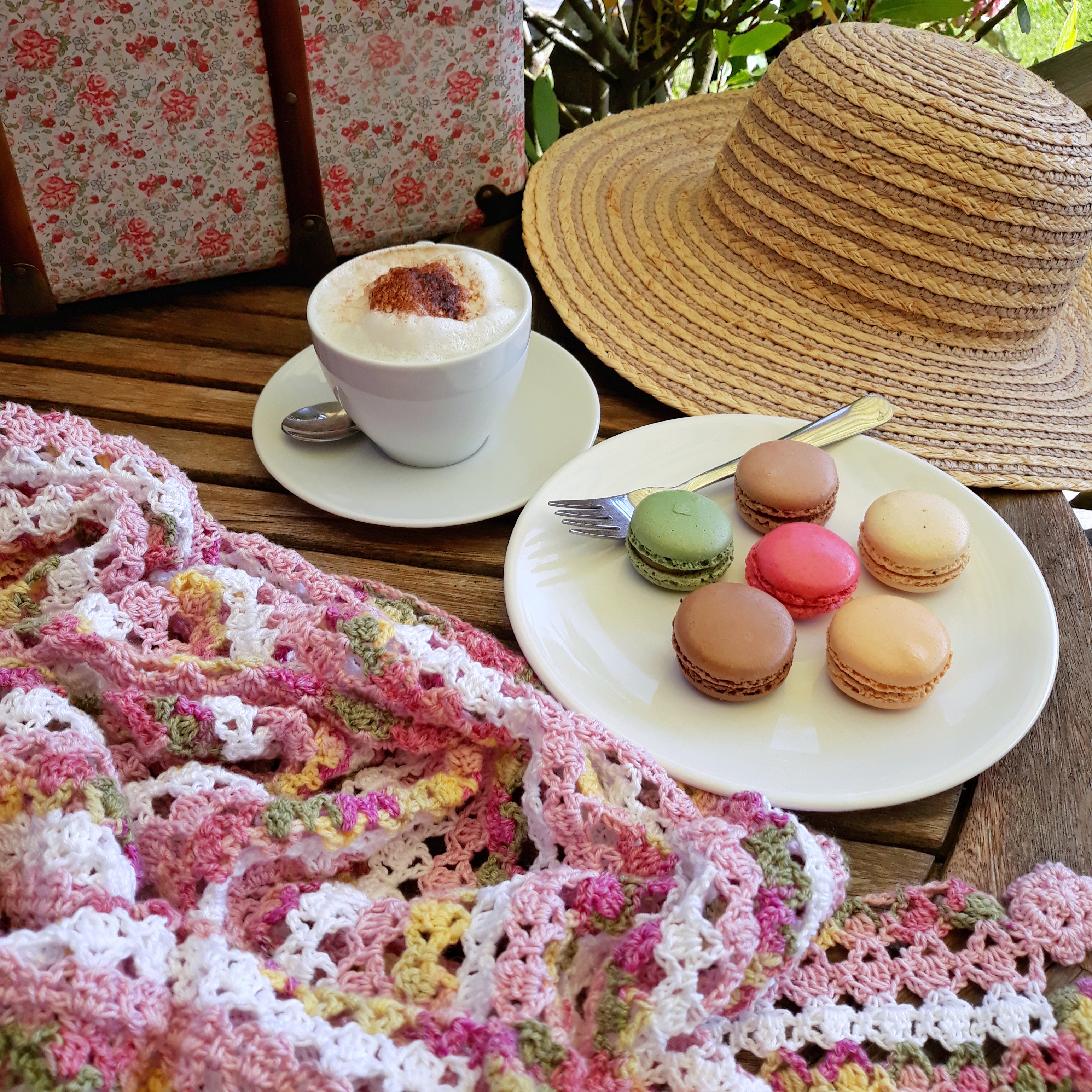 Häkeltuch vor Teller mit Macarons und Tasse mit Milchkaffee