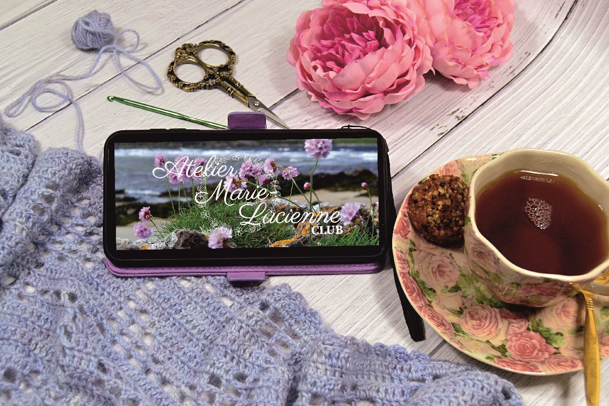 Making of video running on a mobile phone which is lying on a blue crochet scarf next to cup of tea