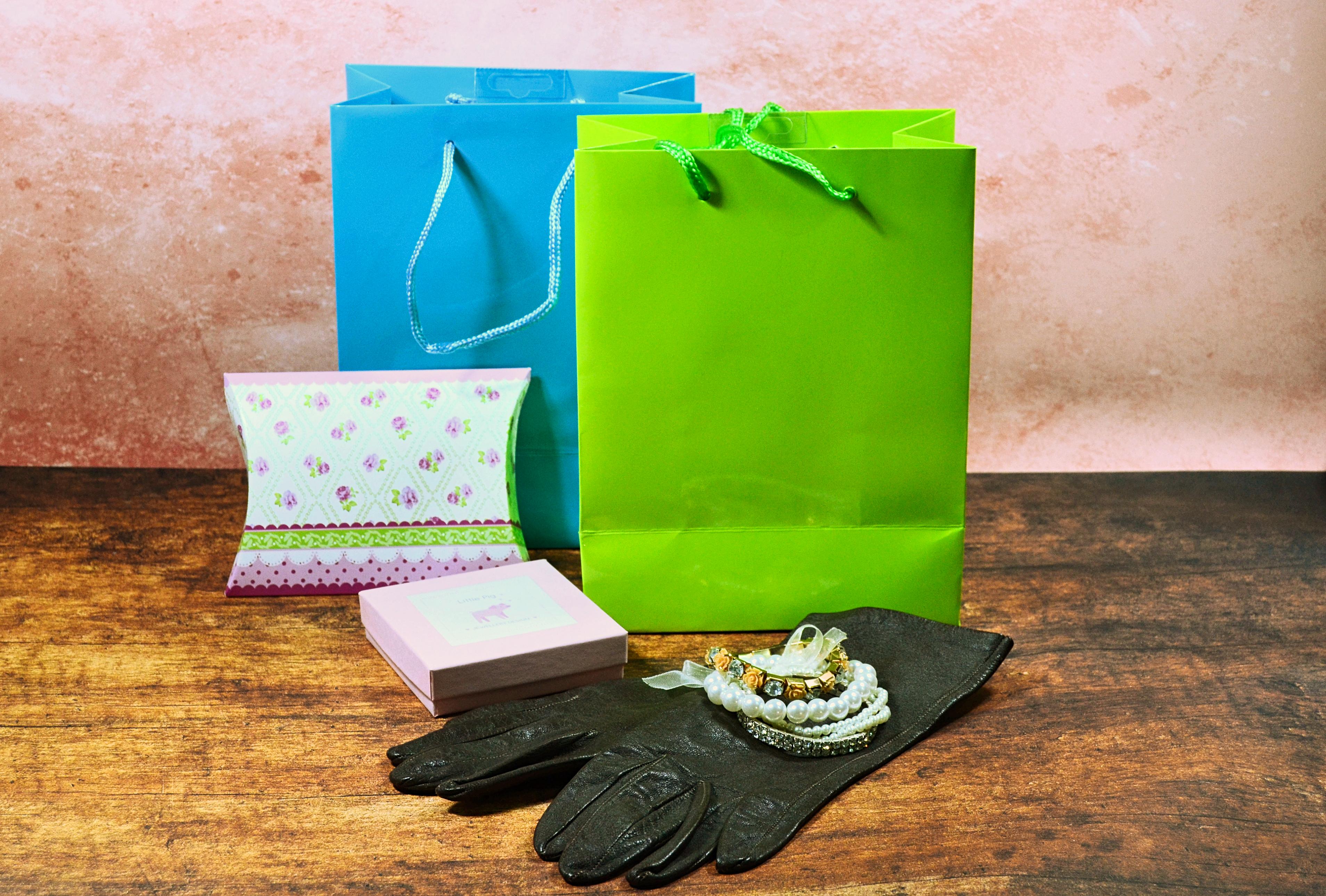 Shopping bags in blue and green and pink boxes next to leather gloves