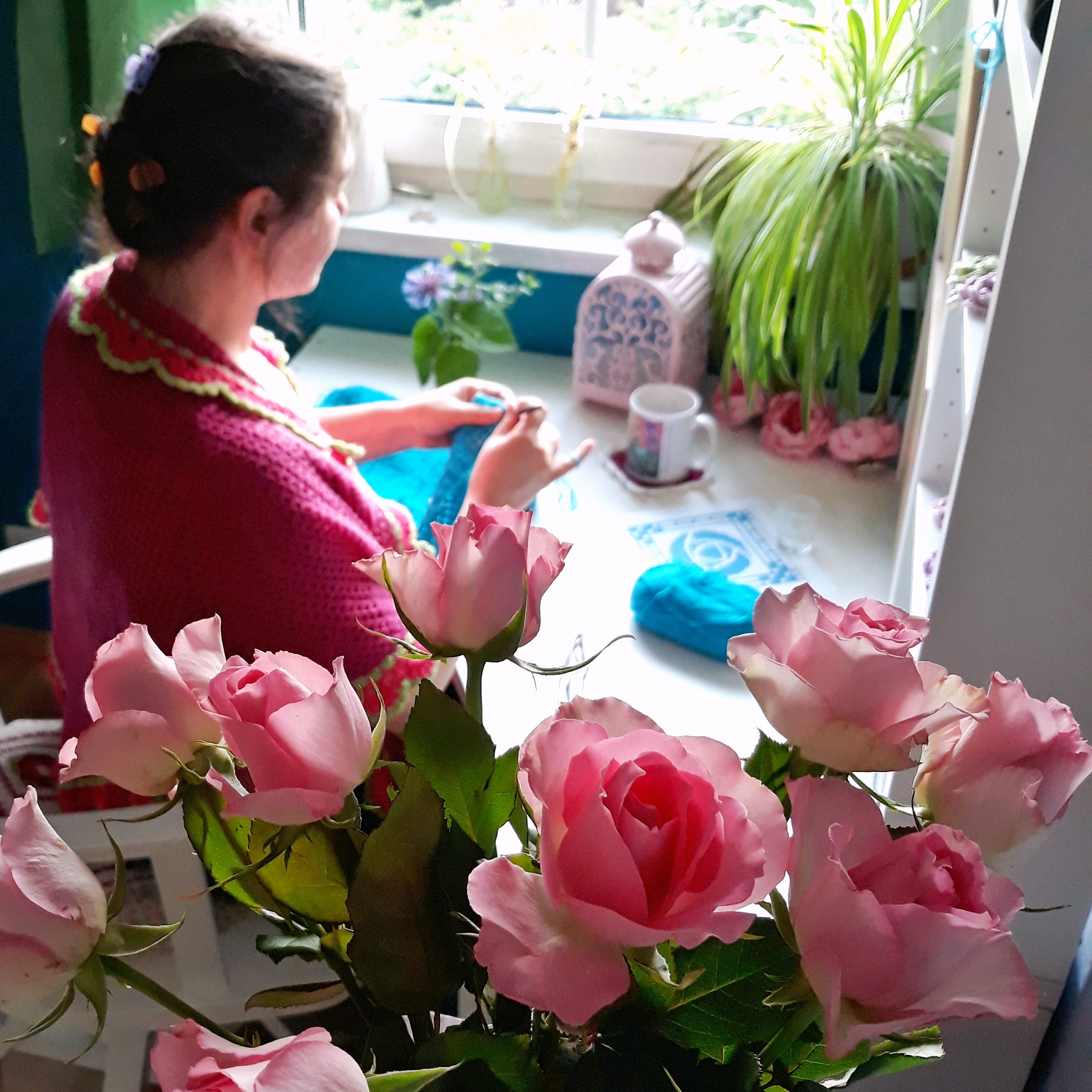 A woman sitting at the table crocheting with blue yarn